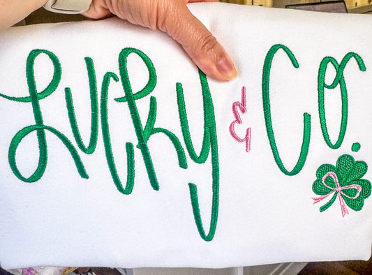 White Gildan Softstyle Sweatshirt with an embroidered design that says "Lucky & Co." with a cute shamrock and bow accent. The wording is all in the color green, except for the "&" and the bow, which are in pink. Very cute shirt for St.Patrick's Day festivities.