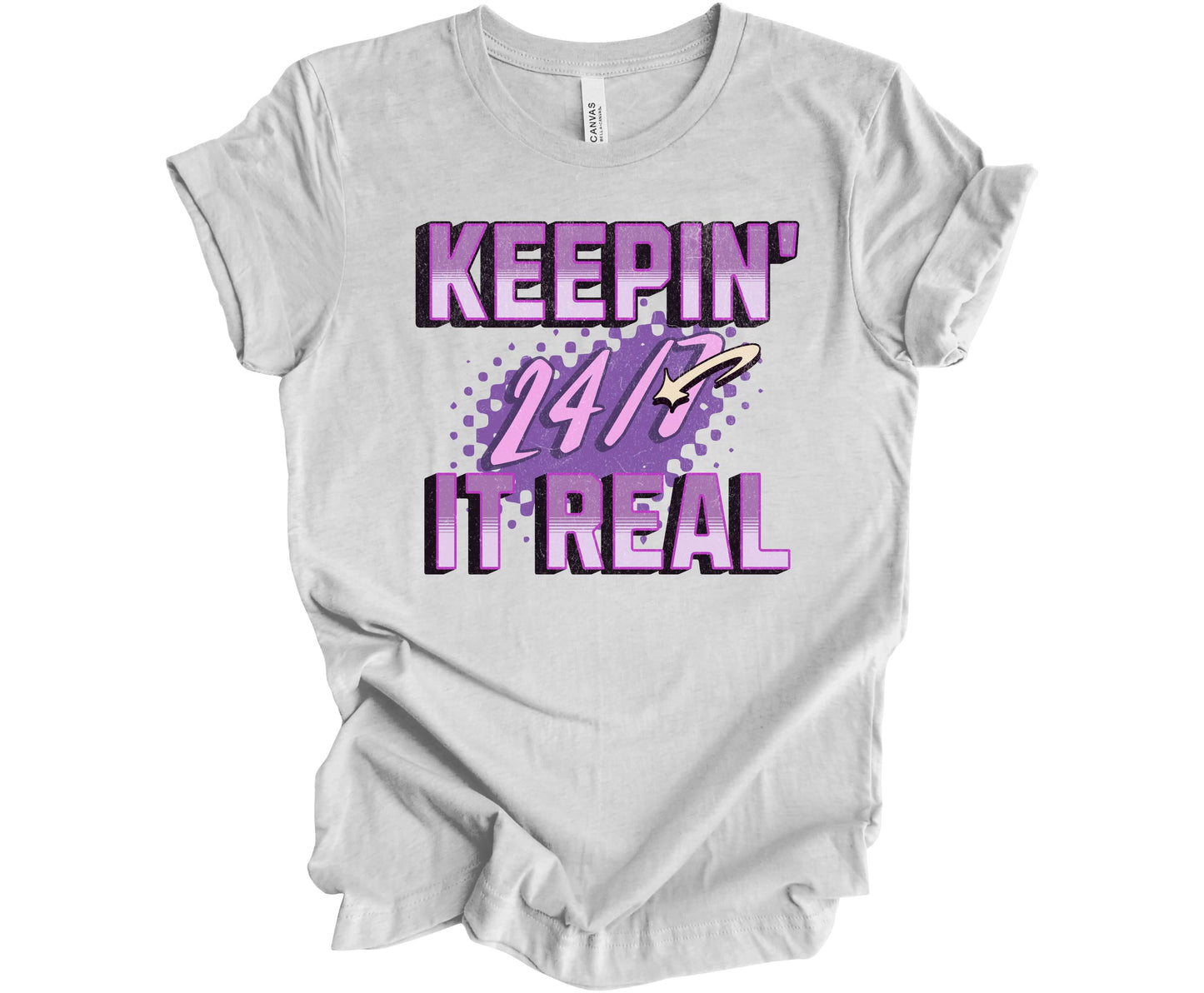 Bella Canvas T-shirt in the color Ash with the words Keepin' It Real 24/7 in different shades of purple with a 3D effect