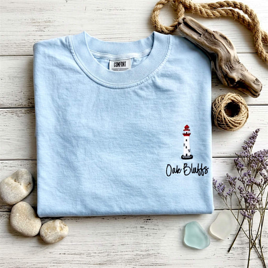 Lifestyle image of our embroidered Comfort Colors Lighthouse t-shirt styled with a coastal-inspired aesthetic. Personalized with Oak Bluffs as an example from our Coastal Collection.