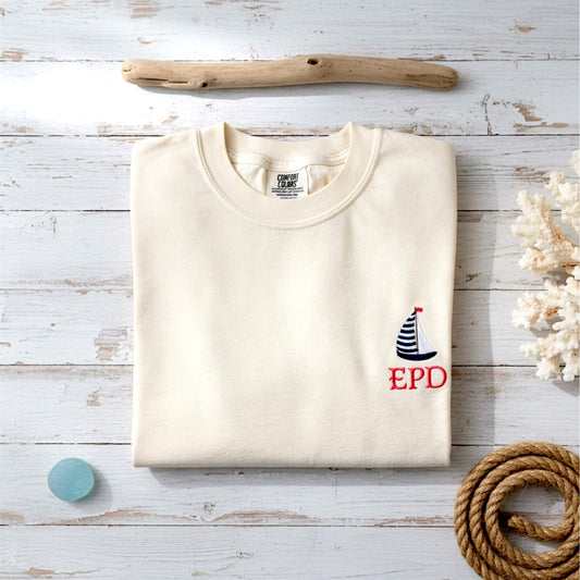 Lifestyle image of our embroidered Comfort Colors sailboat t-shirt styled with a coastal-inspired aesthetic. Personalized with your initials as an example from our Coastal Collection.
