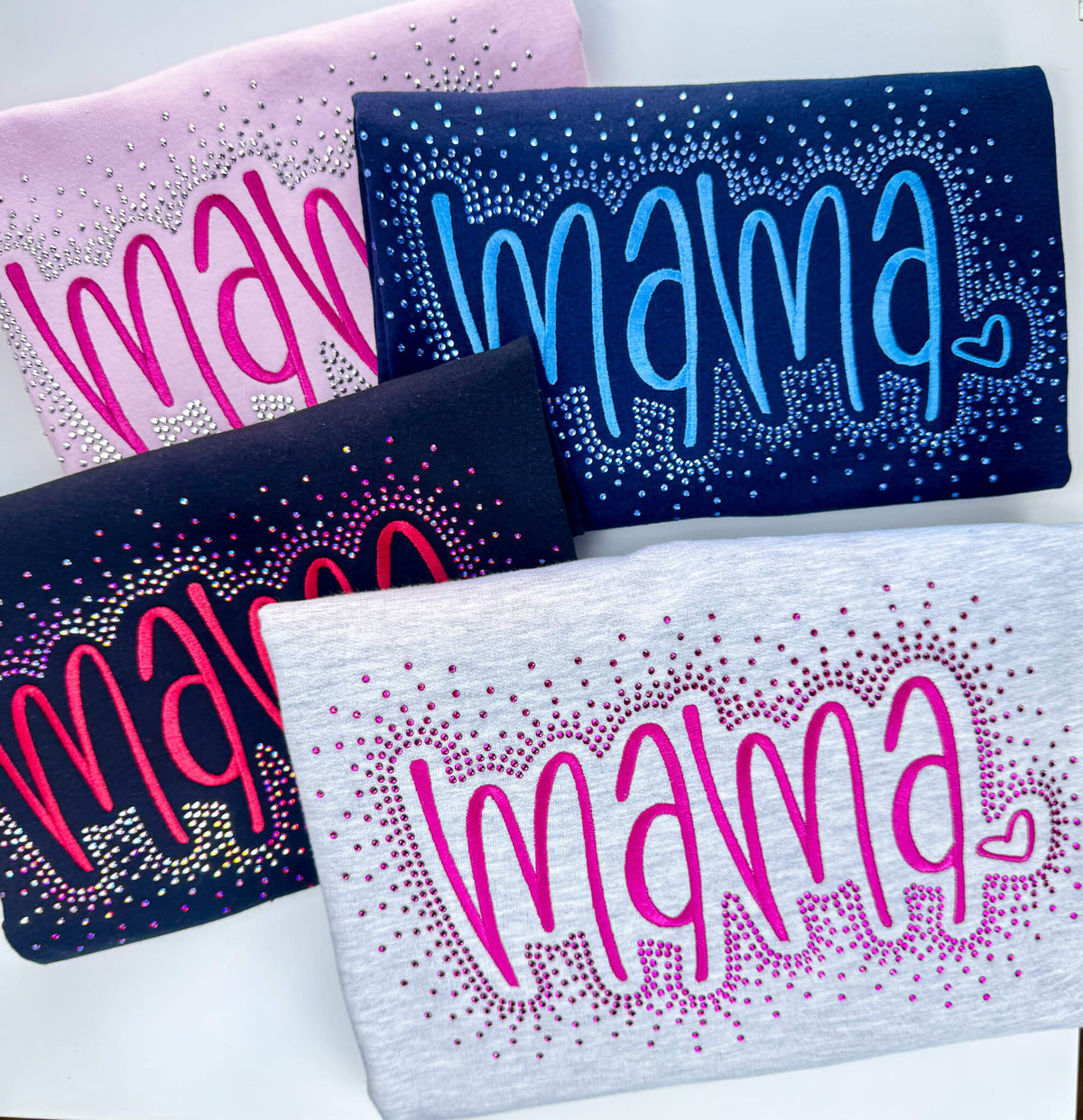This listing is for a Gildan Softstyle Sweatshirt with the word "MAMA" embroidered in a large font.  The sweatshirt colors offered are:  1) Ash Gray with hot pink stitching, 2) Black with red stitching, 3) Lt Pink with pink stitching and 4) Navy with medium blue stitching.  Each shirt comes with the option of adding a rhinestone splatter around the embroidery in a complimentary color.  This image shows each color offered with the rhinestone splatter.