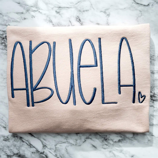 Gildan T-Shirt in the color Dusty Rose with the word "Abuela" embroidered in a large handwritten font.  The color of the thread compliments the shirt color.