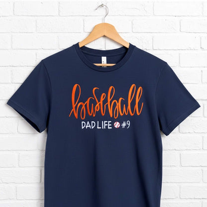Gildan navy blue T-shirt embroidered with the following:  the word "Baseball" in a large script handwritten font, with the tag line Dad Life and a cute heart.  You have the option to pick your shirt color, add a jersey number and pick a thread color for the word baseball to coordinate with your team's colors.