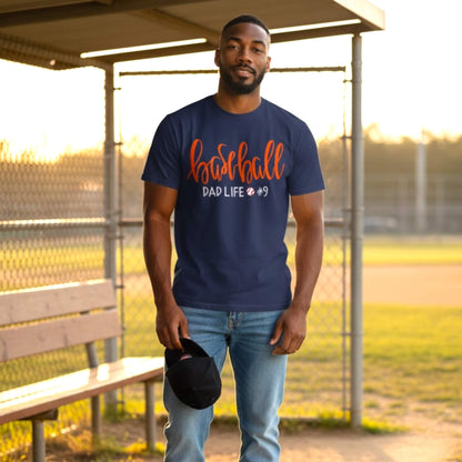 Model wearing a Gildan navy blue T-shirt embroidered with the word "Baseball" in a large script handwritten font, with the tag line Dad Life and his child's jersey number.