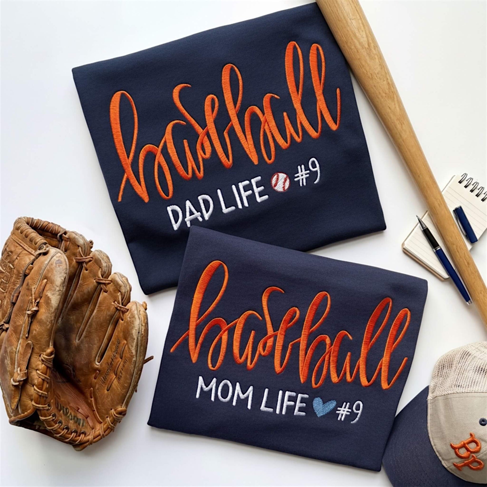 Collage of two embroidered Gildan Navy blue T-shirts.  One is for the baseball moms out there and the other one is for all the die hard baseball dads.  One design reads:  Baseball Mom Life with a cute heart, while the other shirt says Baseball Dad Life with a cute baseball.  You have the option to pick your shirt color, add a jersey number and pick a thread color for the word baseball to coordinate with your team's colors.