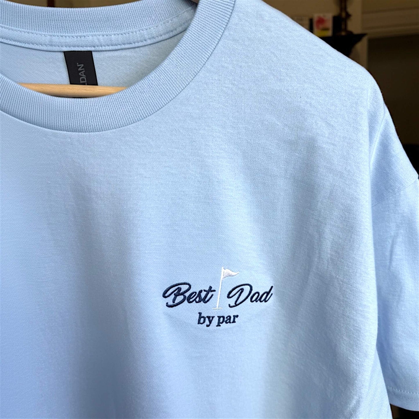 Close up image of a Gildan Light Blue T-Shirt with a left chest embroidered design that says: "Best Dad by Par" with a golf flag.