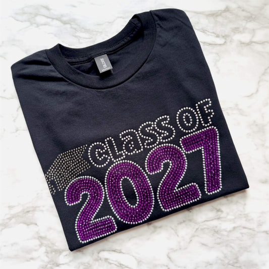 Close up of Class of 2027 rhinestone shirt with Electric Purple and Crystal lettering and graduation cap in black diamond rhinestones.  Design is offered on either a Bella Canvas or Gildan Softstyle black T-shirt.