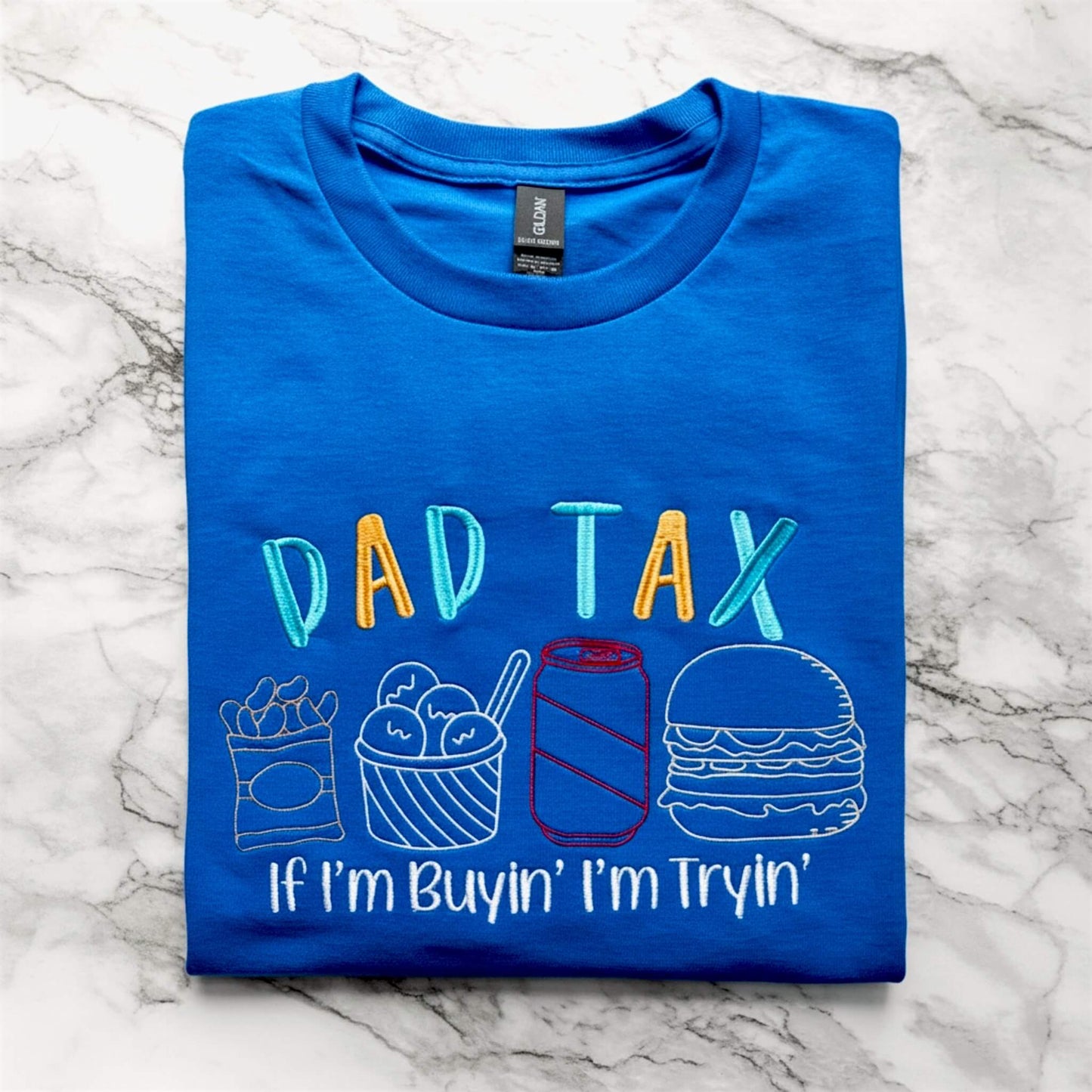 Gildan Royal Blue T-shirt embroidered with a design that says Dad Tax across the top and then four different food outline shapes underneath, with the tag line that says If I'm Buyin' I'm tryin'