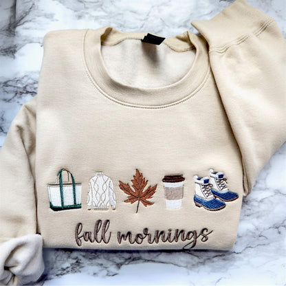 Fall Mornings embroidered sweatshirt with cozy fall-inspired icons on a Gildan Softstyle sweatshirt in the color Sand.