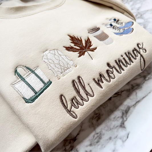 Close up view of our Fall Mornings embroidered sweatshirt with cozy fall-inspired icons on a Gildan Softstyle sweatshirt in the color Sand.