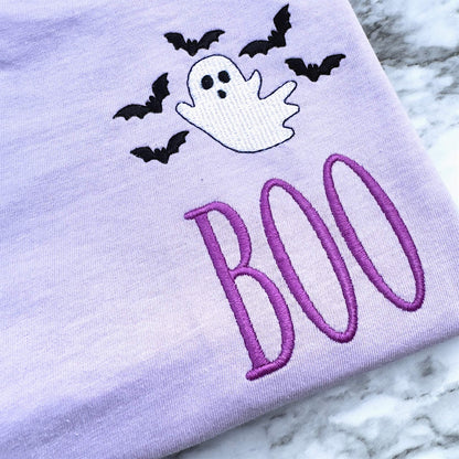 Close-up of embroidered ghost, bats and BOO Halloween design showing detailed stitching.  Design is on a Comfort Colors T-shirt in the color Orchid.
