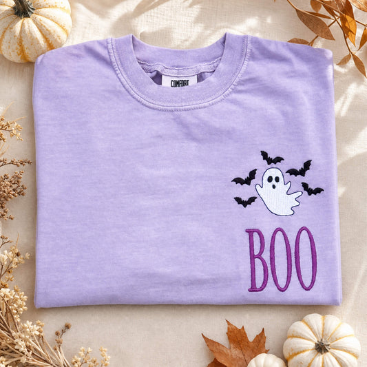 Ghost and bats BOO embroidered Halloween design on a Comfort Colors tee in the color Orchid styled with fall decorations.