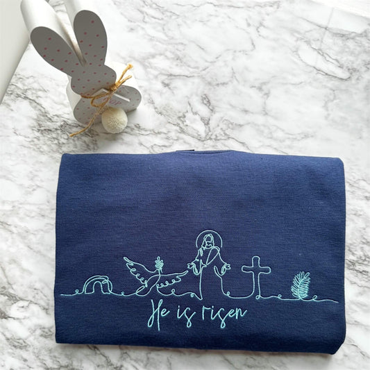 Gildan Softstyle Midweight T-Shirt in the color Navy with Christian symbolic line art and the words "He is risen" - all embroidered in a light blue thread.