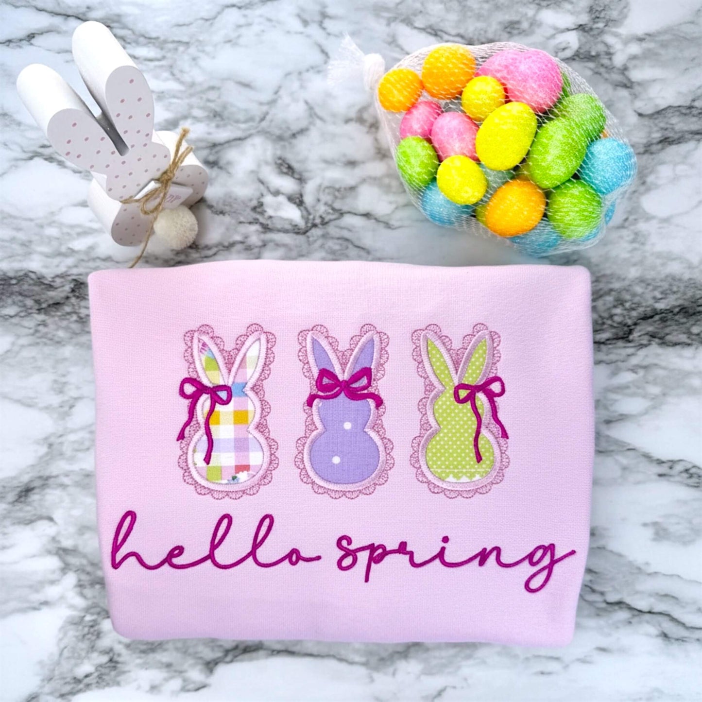 Embroidered Gildan Softstyle Pink Sweatshirt with 3 applique bunnies featuring spring fabric colors, cute coquette bows and the words "hello spring" in a script font.