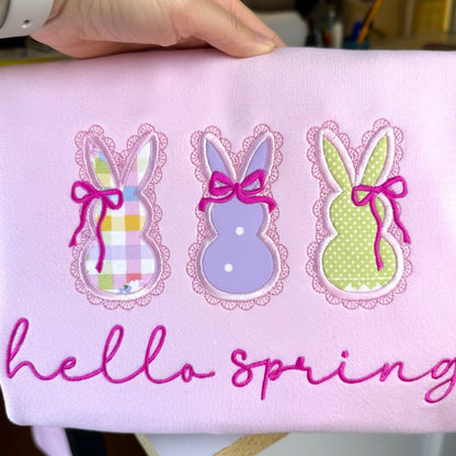 Embroidered Gildan Softstyle Pink Sweatshirt with 3 applique bunnies featuring spring fabric colors, cute coquette bows and the words "hello spring" in a script font.
