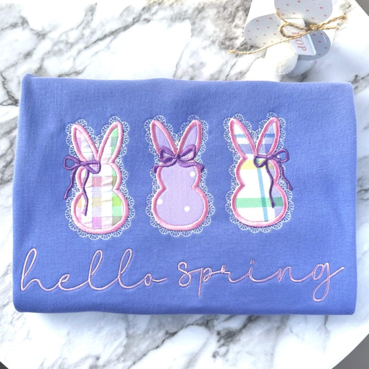 Embroidered Gildan T-Shirt in the color Violet with 3 applique bunnies featuring spring fabric colors, cute coquette bows, delicate lace border and the words "hello spring" in a script font.