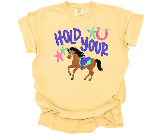 Comfort Colors T-shirt in the color Butter with a colorful graphic design that has the words:  "Hold Your", with a cute horse for the saying "Hold Your Horses".