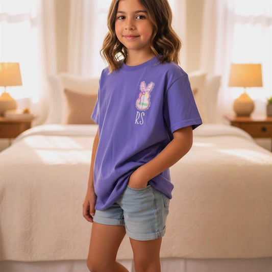 Picture showing a child wearing a Gildan Embroidered T-Shirt in the color Violet with a cute applique bunny on the left chest, featuring a delicate lace border and coquette bow and spring colored fabrics.  The shirt can be personalized by adding your child's initials underneath the bunny.