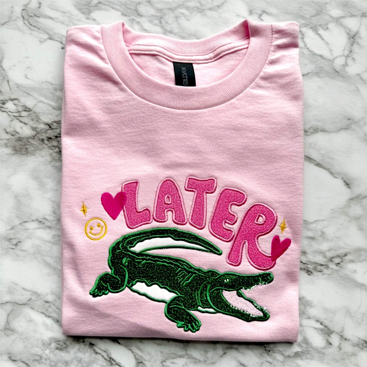 Gildan Light Pink T-Shirt with an applique embroidered design with the word "Later" and an alligator underneath it as a throw back to the old school saying "See ya later alligator".  The design uses HTV glitter in the colors pink and green with cute embroidered accents in hot pink and yellow.