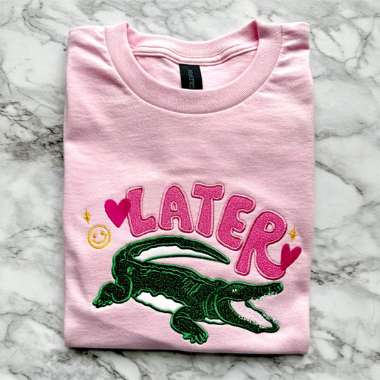 Gildan Light Pink T-Shirt with an applique embroidered design with the word "Later" and an alligator underneath it as a throw back to the old school saying "See ya later alligator".  The design uses HTV glitter in the colors pink and green with cute embroidered accents in hot pink and yellow.