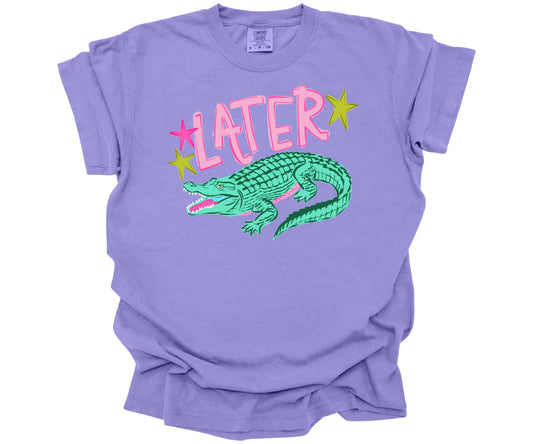 Comfort Colors Tee in the color Violet with a cute nostalgic graphic that is reminiscent of the saying: "See ya later alligator".  The design has the word Later surrounded with stars and an alligator underneath.