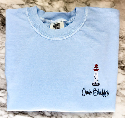 Hydrangea Comfort Colors t-shirt featuring a left chest embroidered lighthouse with "Oak Bluffs" personalization. Part of our Coastal Collection, this customizable embroidered tee can be personalized with your favorite beach town, island, or coastal destination, such as Cape Cod, Nantucket, or Long Island, and is available in five coastal-inspired colors.