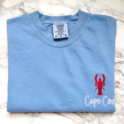 Comfort Colors t-shirt featuring a left chest embroidered lobster with the words Cape Cod.  Part of our Coastal Collection, this customizable embroidered tee can be personalized with your favorite beach town, island, coastal destination, or initials (sailboat design only) and is available in five coastal-inspired colors.