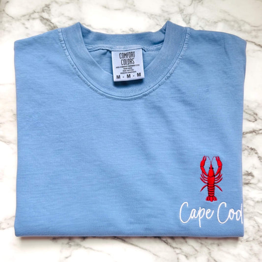 Comfort Colors t-shirt featuring a left chest embroidered lobster with the words Cape Cod.  Part of our Coastal Collection, this customizable embroidered tee can be personalized with your favorite beach town, island, coastal destination, or initials (sailboat design only) and is available in five coastal-inspired colors.