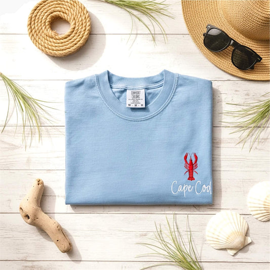 Lifestyle image of our embroidered Comfort Colors lobster t-shirt styled with a coastal-inspired aesthetic. Personalized with the words Cape Cod as an example from our Coastal Collection.