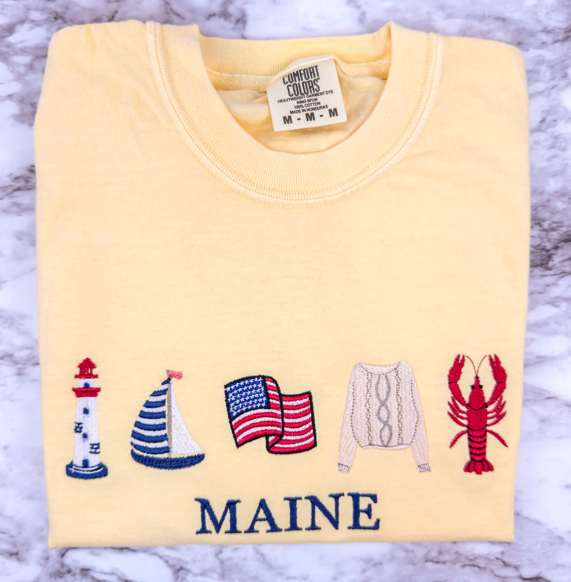Embroidered Comfort Colors t-shirt in the color butter featuring a coastal-inspired design with a personalized custom beach destination text that can be changed to your favorite location.  Part of the Coastal Collection.