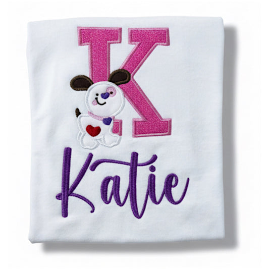 Gildan white Tshirt with a cute valentine personalized design.  The design consists of your child's first initial in a pink glitter HTV with pink stitching.  A cute adorable puppy stands in front of the letter.  You can then embroider your child's name on the bottom in the color purple.  Font used will be based on the length of the name, but we will try to match the listing as much as possible.  Any changes to the font will require your prior approval.