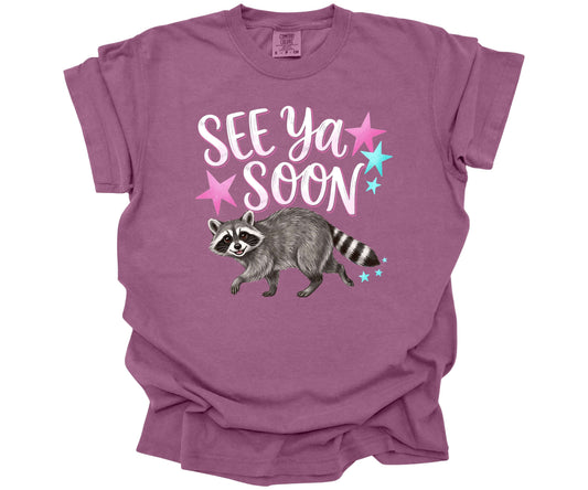 Comfort Colors Tee in the color Berry with a cute funny design.  The design says "See Ya Soon" with a Raccoon underneath the words.