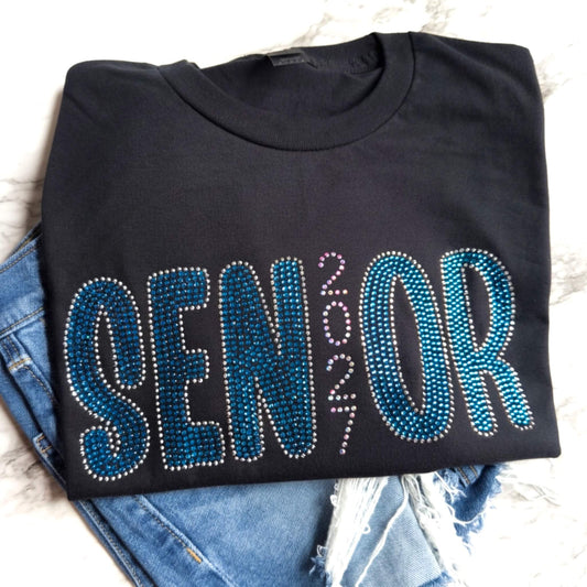 Senior 2027 rhinestone shirt in the color black with Capri, Chrome and Crystal AB rhinestones.  Design can be put on a Bella Canvas or Gildan Softstyle T-Shirt.