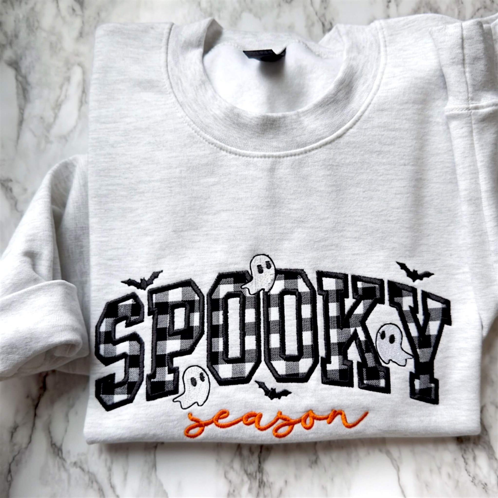 Spooky Season Halloween embroidered design on a Gildan softstyle Ash Gray sweatshirt with checkerboard appliqué, orange script lettering, and cute ghosts and bats.