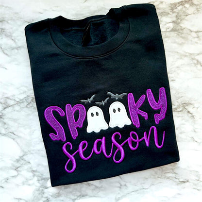 Black Spooky Season Halloween Gildan Softstyle sweatshirt with purple glitter HTV in the word "Spooky" and white glitter inside of the ghosts which replaces the Os in the word Spooky, puff 3D embroidery for the word "Season" and gray bats.