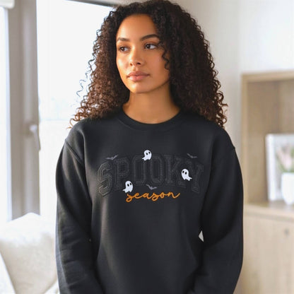 Woman wearing a Gildan Softstyle black Spooky Season Halloween embroidered sweatshirt with black glitter HTV applique, orange script lettering, ghosts and bats.