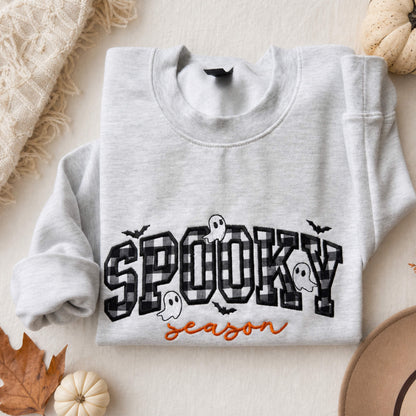 Spooky Season Halloween embroidered design on a Gildan Softstyle Ash Gray sweatshirt with checkerboard appliqué, orange script lettering, and cute ghosts and bats styled in a cozy fall flat lay with seasonal decor.