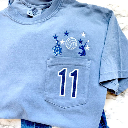 Personalized Comfort Colors Blue Jean volleyball pocket tee with embroidered volleyball design, custom jersey number in blue glitter HTV, and permanently closed pocket.